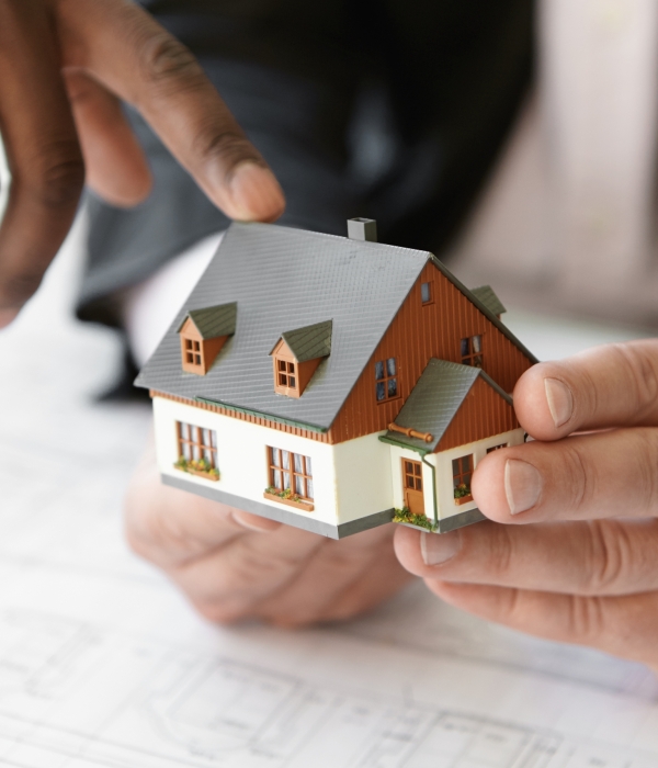 Close up shot of Caucasian contractor holding real estate project while his African colleague pointing finger at scale model building, explaining design during presentation meeting in office